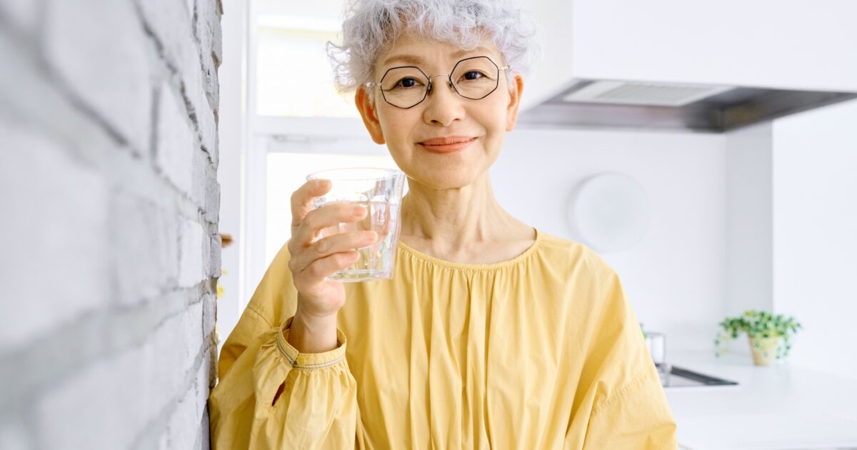 キッチンで水を飲む白髪の女性